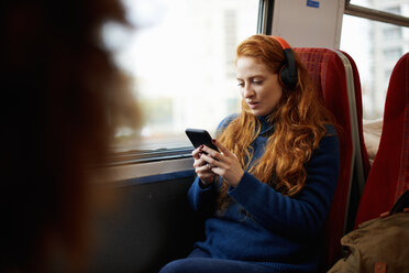 Frau im Zug, die mit Kopfhörern Musik auf ihrem Mobiltelefon hört, London - CUF09293