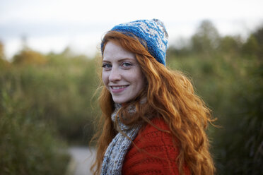Portrait of red haired woman looking over shoulder at camera smiling - CUF09297