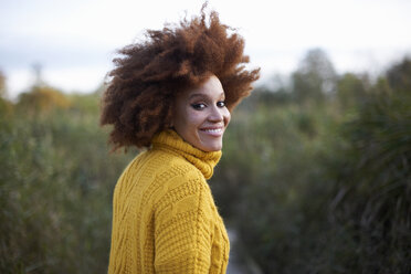 Porträt einer Frau mit Afro, die lächelnd über die Schulter in die Kamera schaut - CUF09298