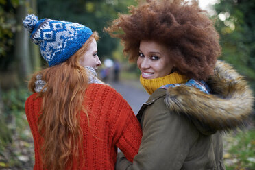 Friends walking arm in arm looking over shoulder at camera smiling - CUF09300