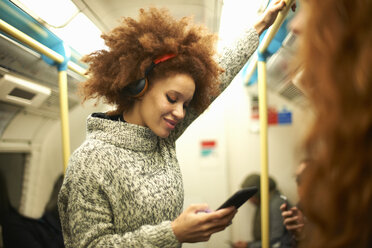 Junge Frau in der U-Bahn, die auf ihr Smartphone schaut - CUF09306