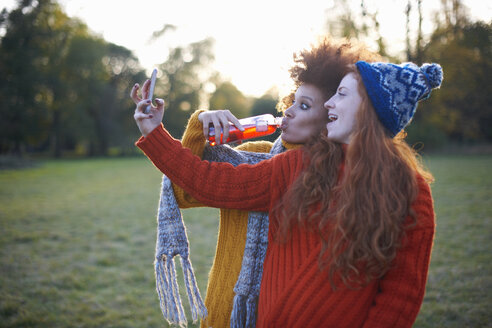 Zwei junge Frauen in ländlicher Umgebung, die ein Selfie mit ihrem Smartphone machen - CUF09339