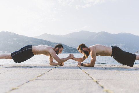 Zwei junge Männer machen Liegestütze am Wasser, Comer See, Lombardei, Italien, lizenzfreies Stockfoto