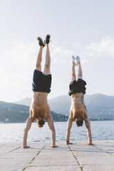 Zwei junge Männer machen Handstände am Ufer, Comer See, Lombardei, Italien - CUF09349