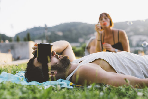 Junger Mann liegt im Gras und schaut durch ein Virtual-Reality-Headset, Como, Lombardei, Italien - CUF09352