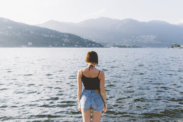 Rückansicht einer jungen Frau am Ufer mit Blick auf den Comer See, Lombardei, Italien - CUF09360