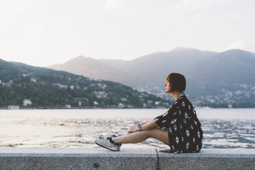 Young woman sitting on waterfront wall at Lake Como, Lombardy, Italy - CUF09361