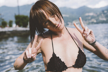 Portrait of young woman in bikini top making peace sign by Lake Como, Lombardy, Italy - CUF09363