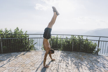 Junger Mann im Handstand auf einer Aussichtsplattform, Comer See, Lombardei, Italien - CUF09375