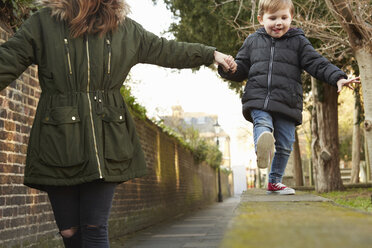 Frau, die die Hand ihres kleinen Sohnes hält, läuft auf einer Straßenmauer - CUF09578