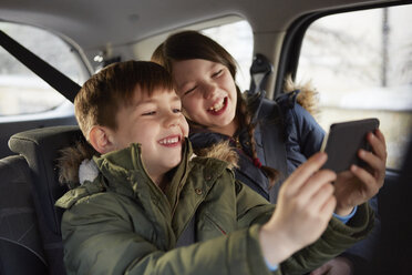 Junge und Schwester machen lachendes Selfie auf dem Rücksitz eines Autos - CUF09583