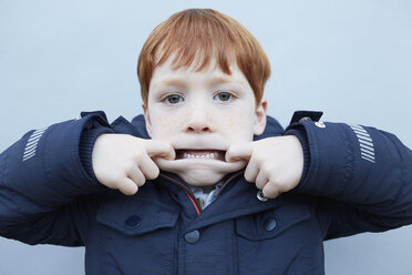 Portrait of red haired boy in front of wall pulling a face - CUF09594