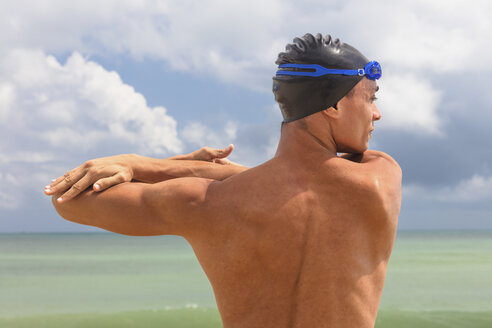Rückansicht eines muskulösen männlichen Schwimmers am Strand beim Aufwärmen - CUF09603
