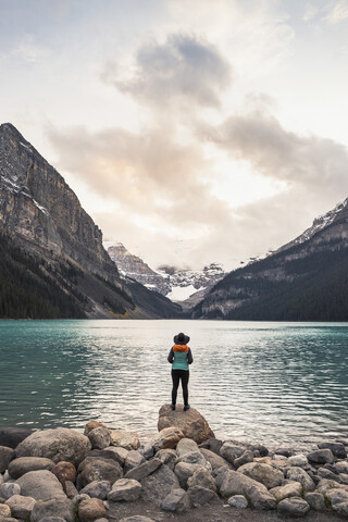 Frau auf einem Felsen stehend, Blick auf den See, Rückansicht, Lake Louise, Alberta, Kanada, lizenzfreies Stockfoto