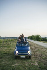 Tourists standing through car sunroof, vineyard, Tuscany, Italy - CUF09686