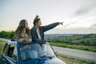 Tourists standing through car sunroof, countryside, Tuscany, Italy - CUF09688