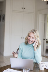 Smiling mature woman with credit card talking on telephone at laptop - HOXF03542