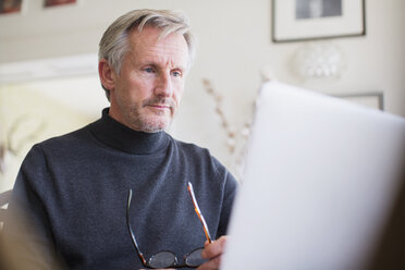 Fokussierter reifer männlicher Freiberufler, der zu Hause am Laptop arbeitet - HOXF03547