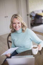 Porträt einer lächelnden, selbstbewussten Freiberuflerin, die zu Hause am Laptop arbeitet und Tee trinkt - HOXF03548