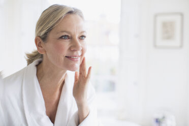 Lächelnde reife Frau, die sich vor dem Badezimmerspiegel mit Feuchtigkeitscreme eincremt - HOXF03553