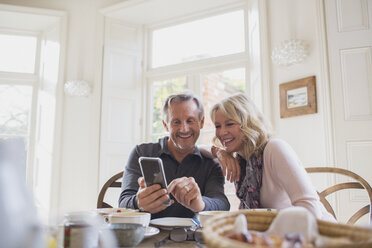 Lächelndes reifes Paar benutzt Smartphone am Esstisch - HOXF03555