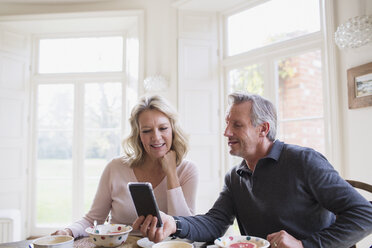 Mature couple using smart phone at breakfast table - HOXF03558