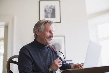 Smiling mature male freelancer working at laptop at home - HOXF03560
