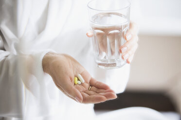 Woman taking vitamins with glass of water - HOXF03608