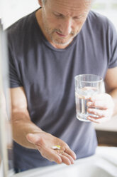 Mature man taking vitamins with glass of water - HOXF03616