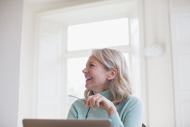 Glückliche reife Freiberuflerin, die zu Hause am Laptop arbeitet - HOXF03618