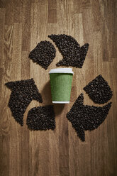Kaffeebohnen, die ein Recyclingsymbol um einen grünen, wiederverwertbaren Kaffeebecher bilden - CAIF20540