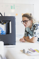 Female designer watching 3D printer in office - CAIF20575