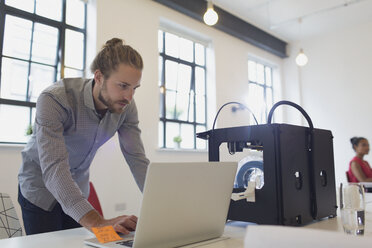 Männlicher Designer arbeitet an einem Laptop neben einem 3D-Drucker im Büro - CAIF20615