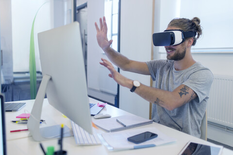 Männlicher Computerprogrammierer, der eine Virtual-Reality-Simulator-Brille am Computer im Büro programmiert, lizenzfreies Stockfoto