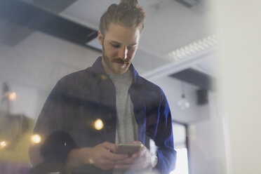 Geschäftsmann, der mit seinem Smartphone im Büro SMS schreibt - CAIF20629