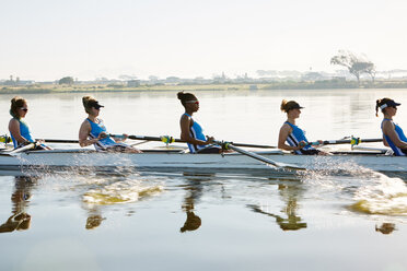 Female rowing team rowing scull on sunny lake - CAIF20655
