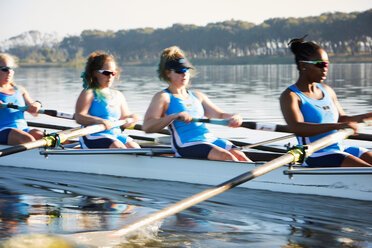 Female rowers rowing scull on sunny lake - CAIF20659