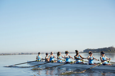 Female rowers rowing scull on sunny lake under blue sky - CAIF20660