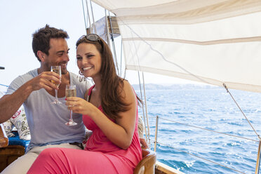 Couple sitting on boat, on water, holding champagne flutes, smiling - CUF09839