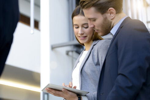 Young businesswoman and man using digital tablet touchscreen in office atrium - CUF09864