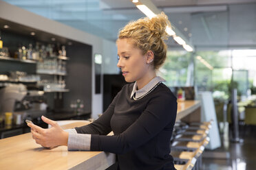 Woman at coffee shop counter using smartphone - CUF09877