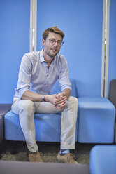 Porträt eines Geschäftsmannes, der auf einem hellblauen Hocker in einem Büro sitzt - BEF00079