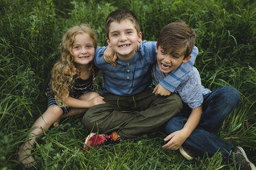Brothers and sister enjoying outdoors on green grassy field - CUF09992