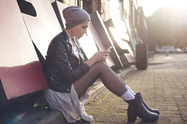 Coole junge Frau sitzt auf der Straße und schaut auf ihr Smartphone - CUF10028