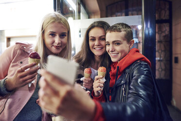 Drei junge Frauen mit Eistüten machen ein Smartphone-Selfie auf einer Straße in der Stadt - CUF10033