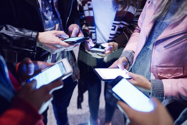 Mid section of young adult friends standing in circle looking at smartphones - CUF10035