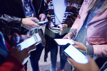 Mittlere Gruppe junger Erwachsener, die im Kreis stehen und auf ihre Smartphones schauen - CUF10035
