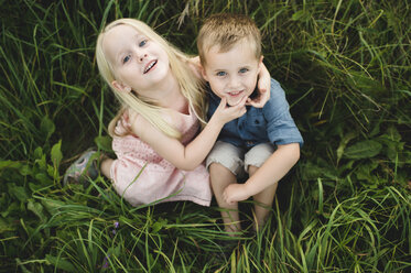 Junge und Mädchen sitzen zusammen im hohen Gras und schauen in die Kamera - CUF10068