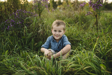 Porträt eines lächelnden Jungen, der im hohen Gras sitzt und in die Kamera schaut - CUF10069