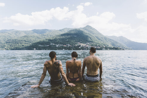 Rückansicht von drei jungen erwachsenen Freunden, die am Comer See sitzen, Como, Lombardei, Italien - CUF10082